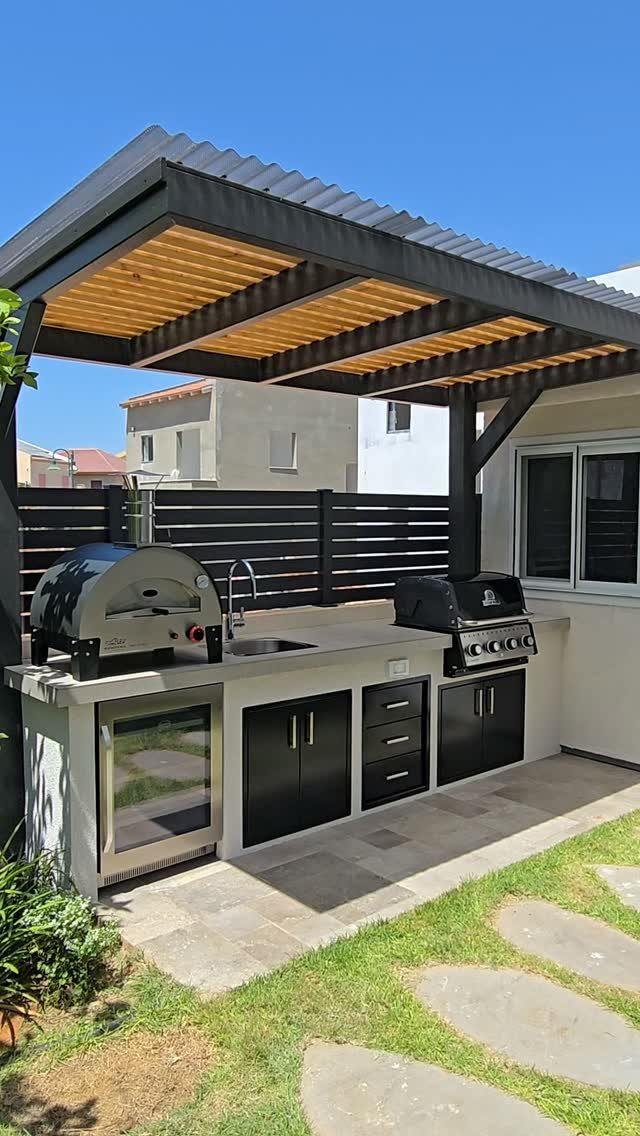 6 Covered Patio Grill Area Ideas for Any Yard 4 Modern outdoor kitchen with built-in grill and sink under a dark metal pergola.