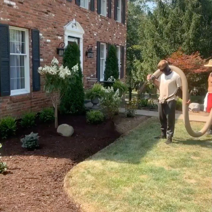 Cozy Winter Garden Ideas: 8 Ways to Warm Cold Months 2 A person spreading dark brown mulch over a garden bed in front of a brick house.