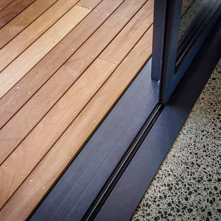 8 Deck No Railing Ideas for Outdoor Living without Barriers 4 Wooden deck planks meeting a dark sliding door track and speckled terrazzo indoor flooring.