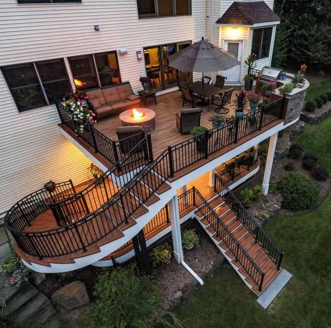 Deck on a Slope: 5 Ideas That Beat the Grade 1 A multi-level wooden deck with black railings, curved stairs, and outdoor furniture attached to a house.