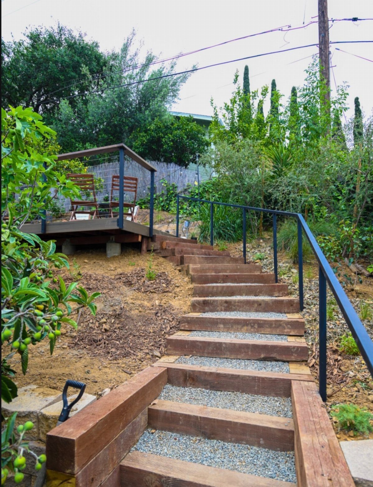 Deck on a Slope: 5 Ideas That Beat the Grade 2 Wooden stairs with gravel infill and metal handrails leading up a sloped garden landscape.