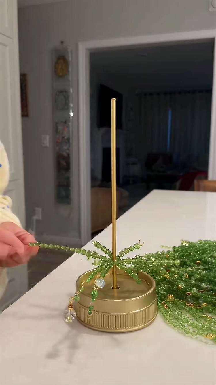 21 DIY Christmas Ornaments for Adults 18 A hand holds a green beaded leaf ornament attached to a gold metal stand.