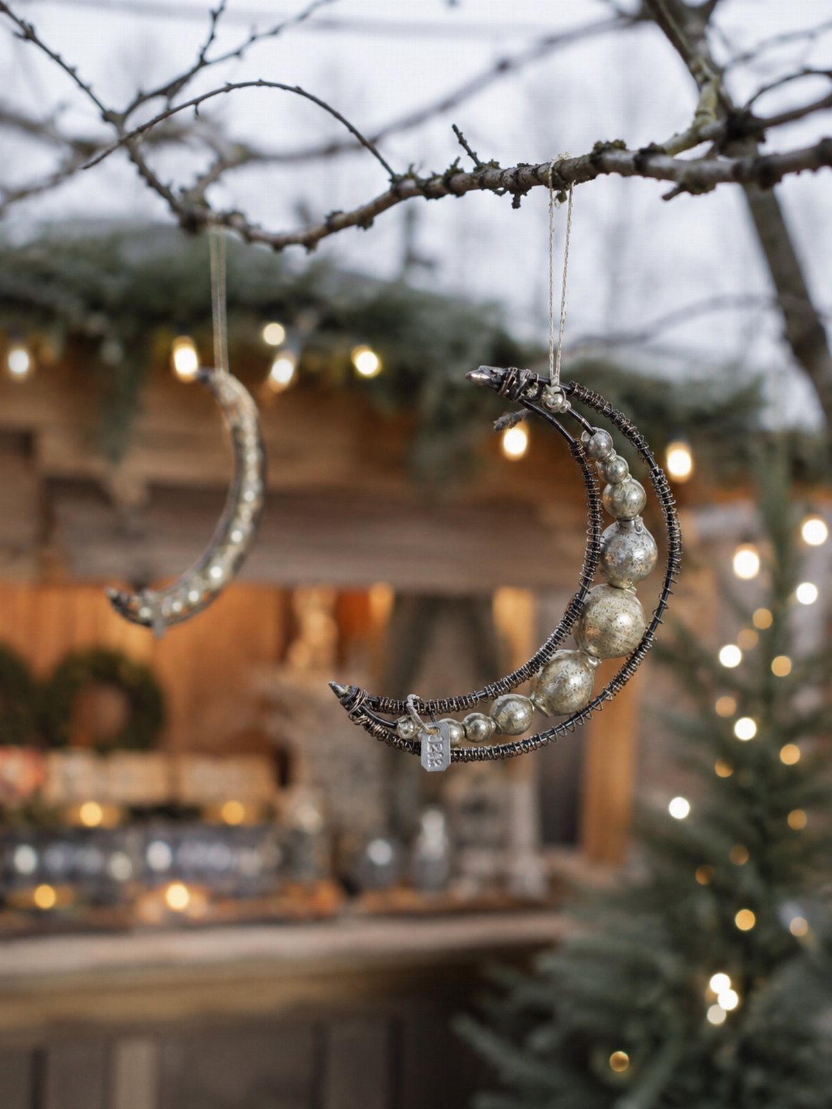 21 DIY Christmas Ornaments for Adults 19 Two beaded crescent moon ornaments hanging from thin tree branches against a blurred background.