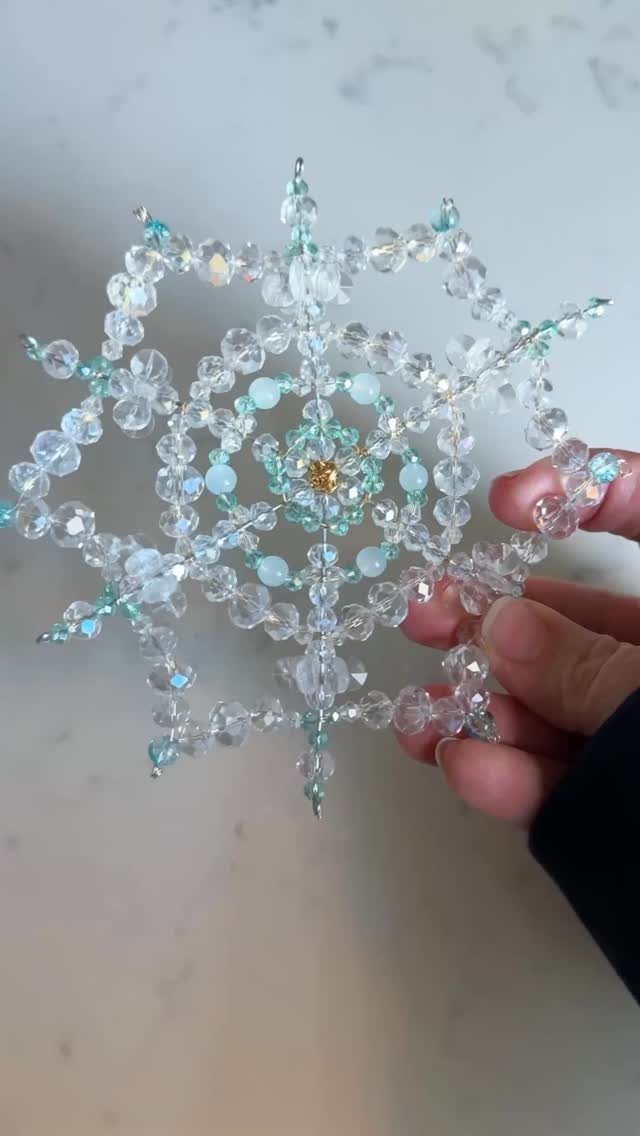 21 DIY Christmas Ornaments for Adults 4 A person holding a large, sparkling snowflake ornament made of clear and teal beads.