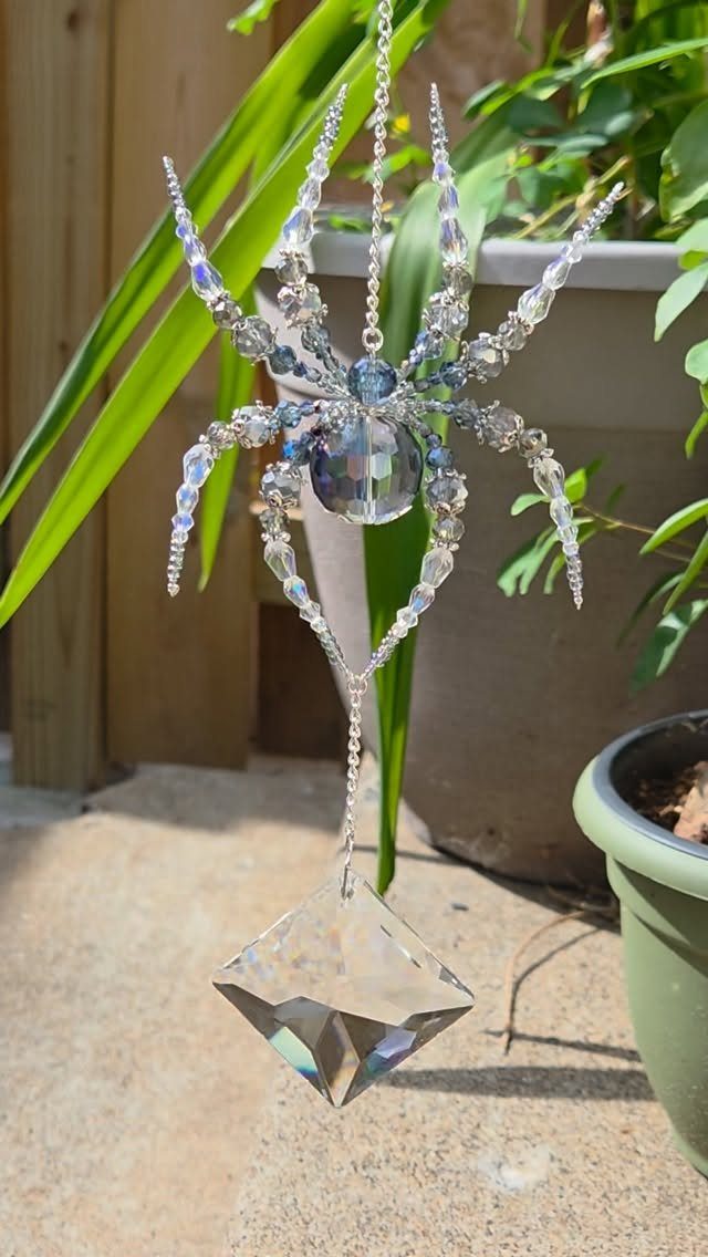 21 DIY Christmas Ornaments for Adults 21 An iridescent beaded spider ornament hanging outdoors near green plants and a stone ground.