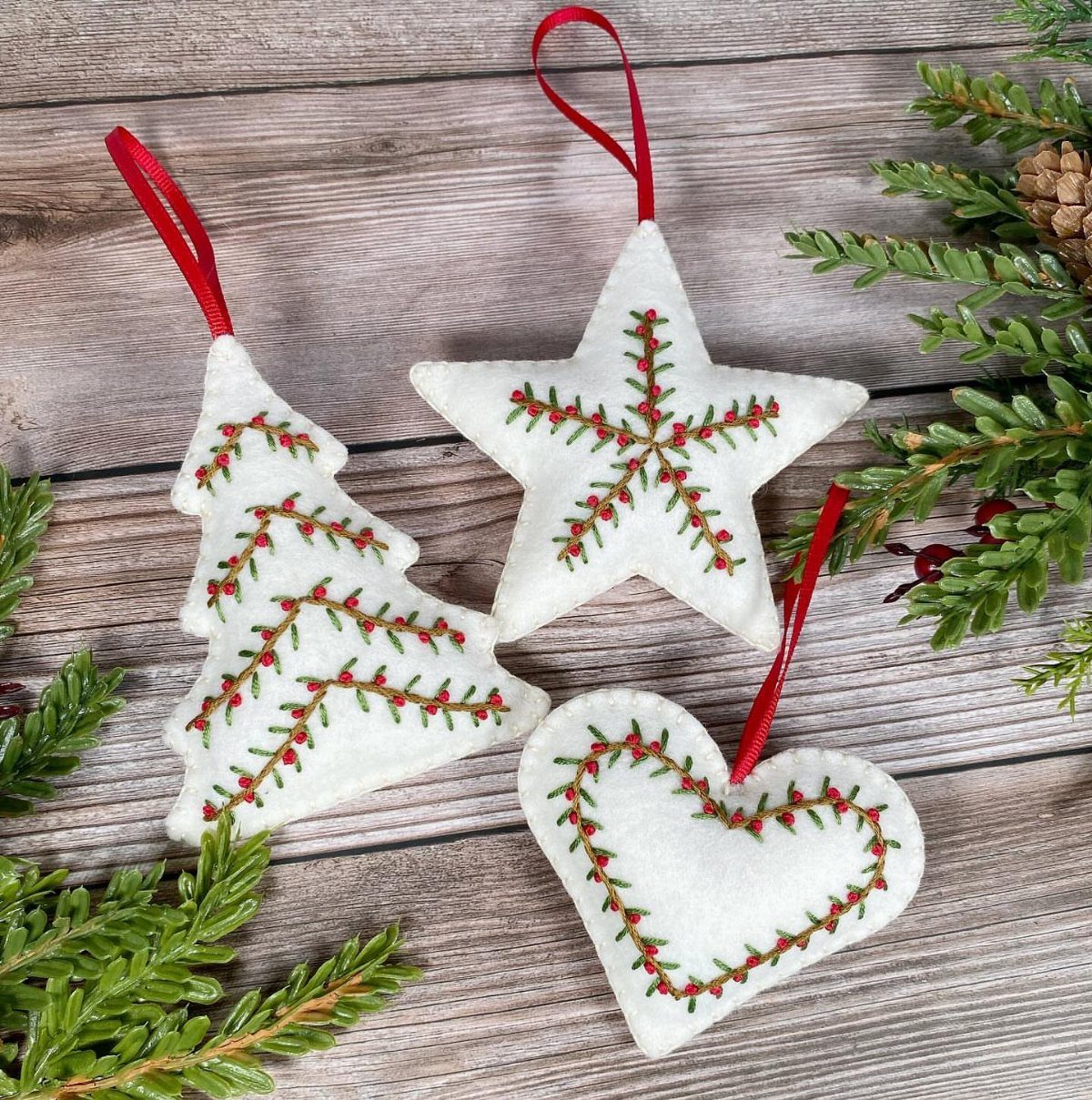 21 DIY Christmas Ornaments for Adults 5 White felt ornaments shaped like a tree, star, and heart with red and green stitching.