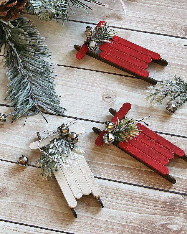 21 DIY Christmas Ornaments for Adults 12 Three popsicle stick sled ornaments with jingle bells and evergreen sprigs on wood.