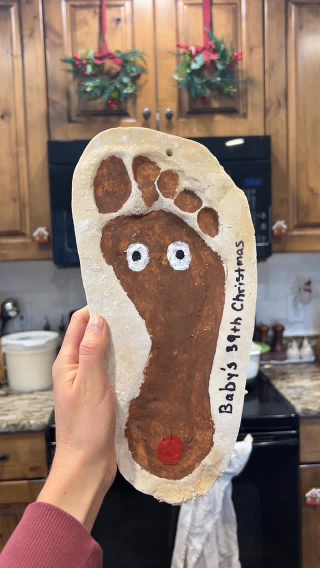 21 DIY Christmas Ornaments for Adults 20 A hand holding a large salt dough ornament shaped like a painted brown footprint.