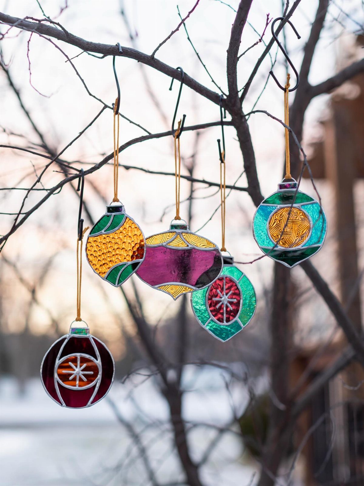 21 DIY Christmas Ornaments for Adults 7 Colorful stained glass effect ornaments hanging from bare tree branches in a winter setting.