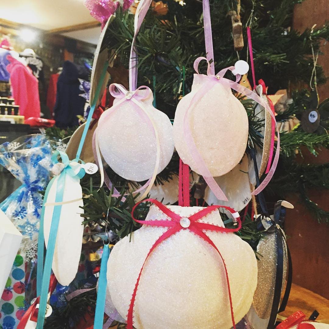 21 DIY Christmas Ornaments for Adults 17 Glittery white round Christmas ornaments with colorful ribbons hanging on a green tree.