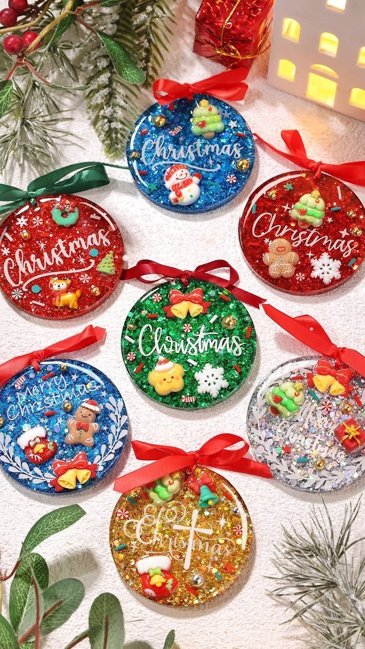 21 DIY Christmas Ornaments for Adults 16 Colorful resin Christmas ornaments with glitter and festive charms resting on a white surface with pine branches.