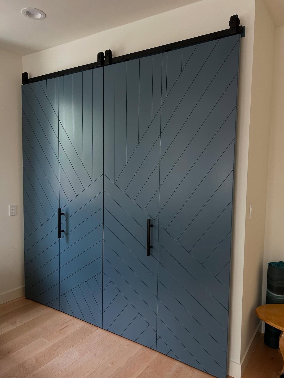 10 DIY Closet Ideas for Room With No Closet 9 Blue-grey chevron patterned barn doors mounted on a black sliding track against a white wall.