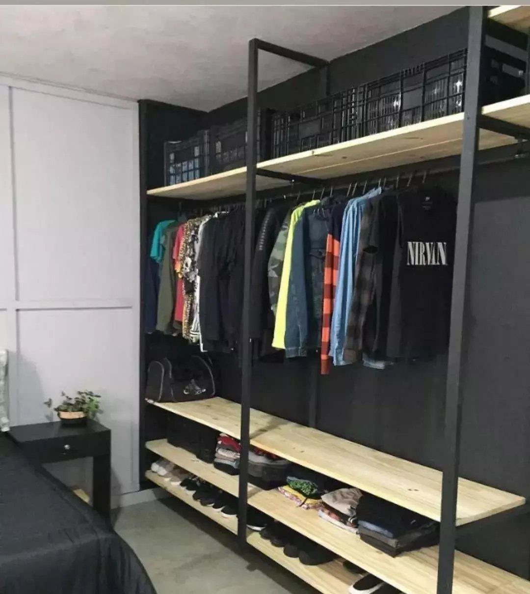 10 DIY Closet Ideas for Room With No Closet 2 Black metal shelving unit with light wood shelves holding folded clothes, shoes, and hanging garments.