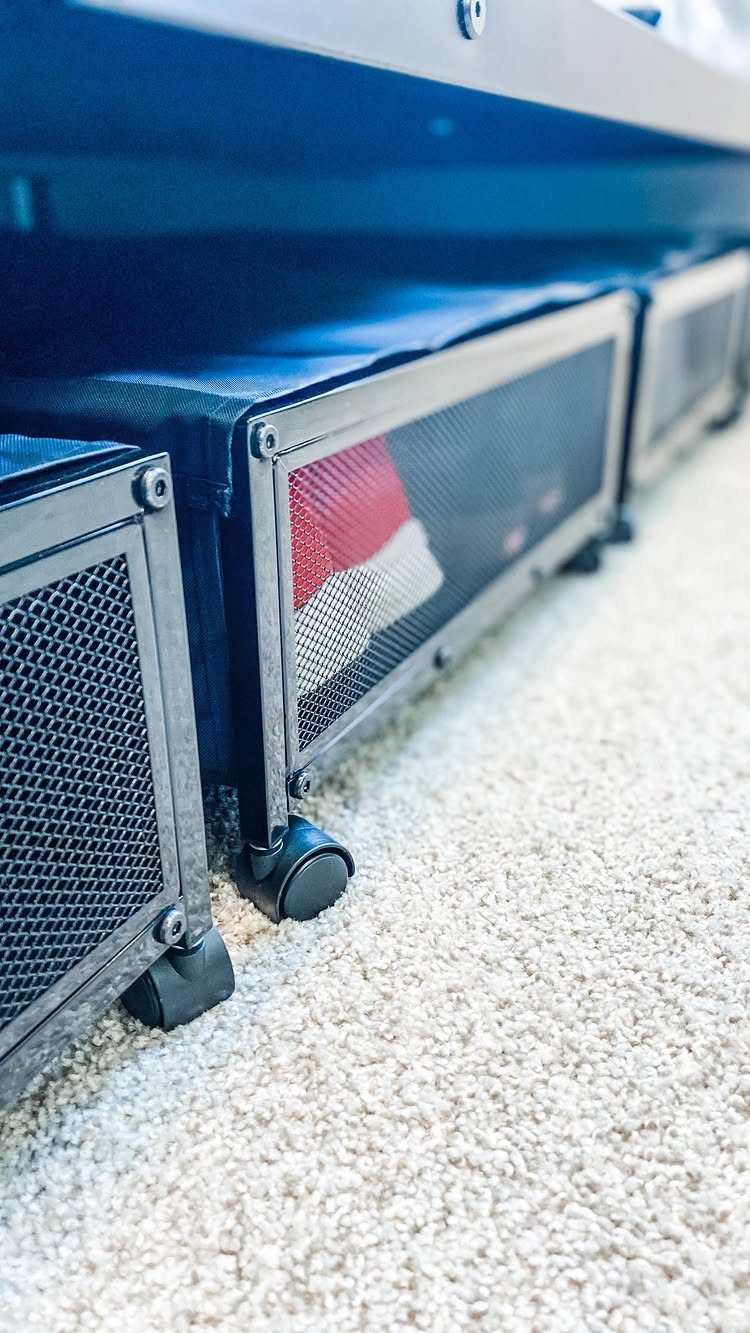 10 DIY Closet Ideas for Room With No Closet 7 Black mesh storage bins with wheels tucked under a bed on a carpeted floor.