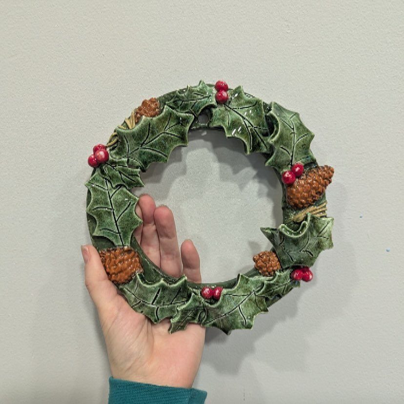 Easy Christmas Clay Ideas: 9 Projects for Handmade Ornaments 4 A hand holding a green ceramic wreath decorated with holly leaves, red berries, and pinecones.