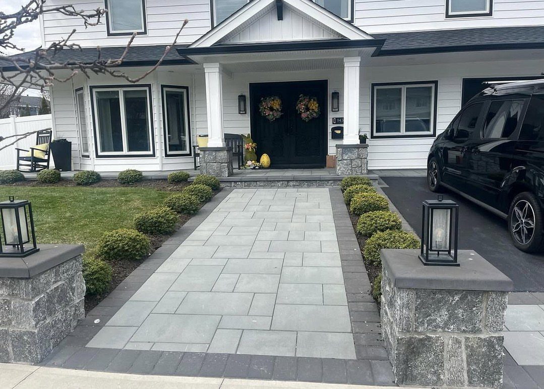 Stone walkway leading to a white house with a black front door and decorative wreaths.
