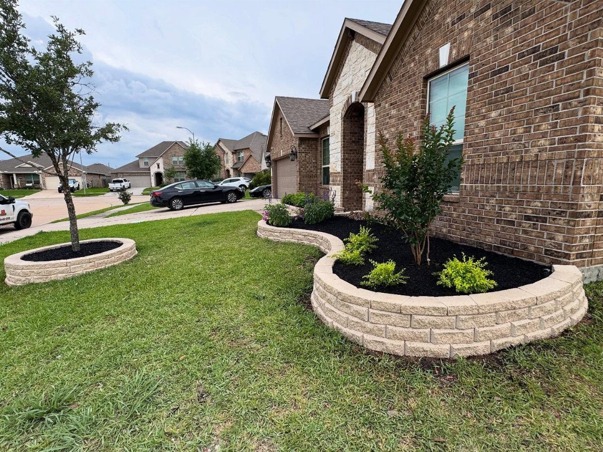 A landscaped front yard with stone-edged garden beds and green shrubs next to a brick house.