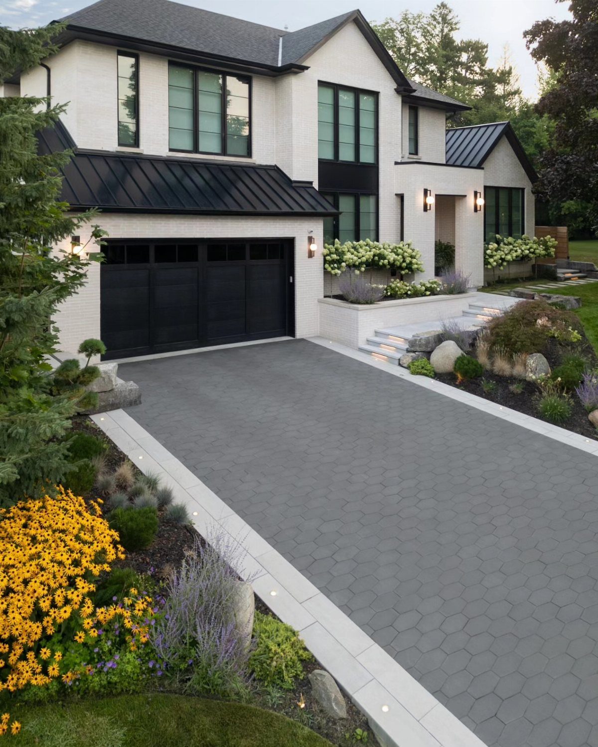 Modern white house with a grey hexagonal paved driveway and landscaped garden beds.