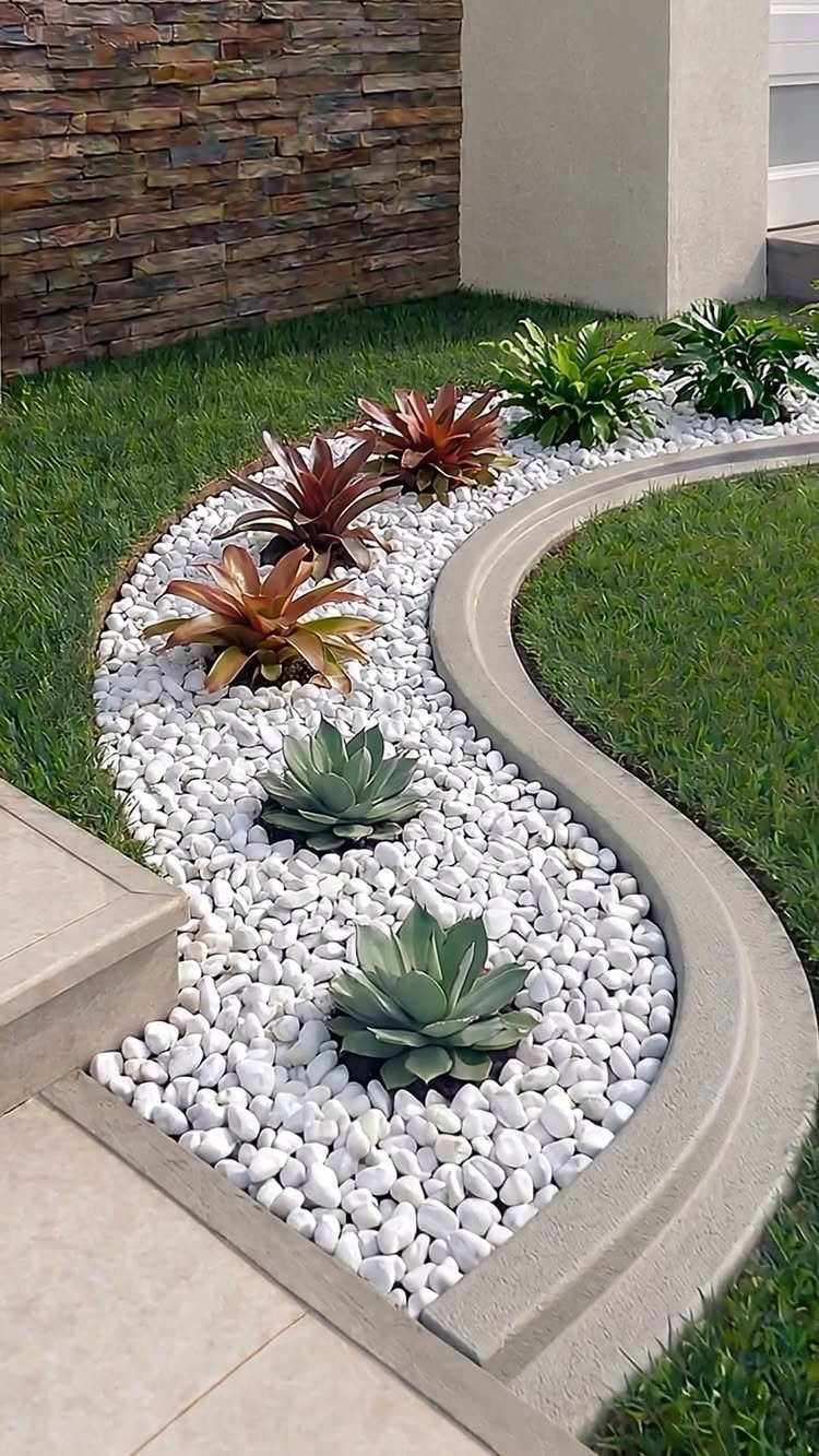 A curved garden bed with white stones and succulents bordered by smooth concrete edging.