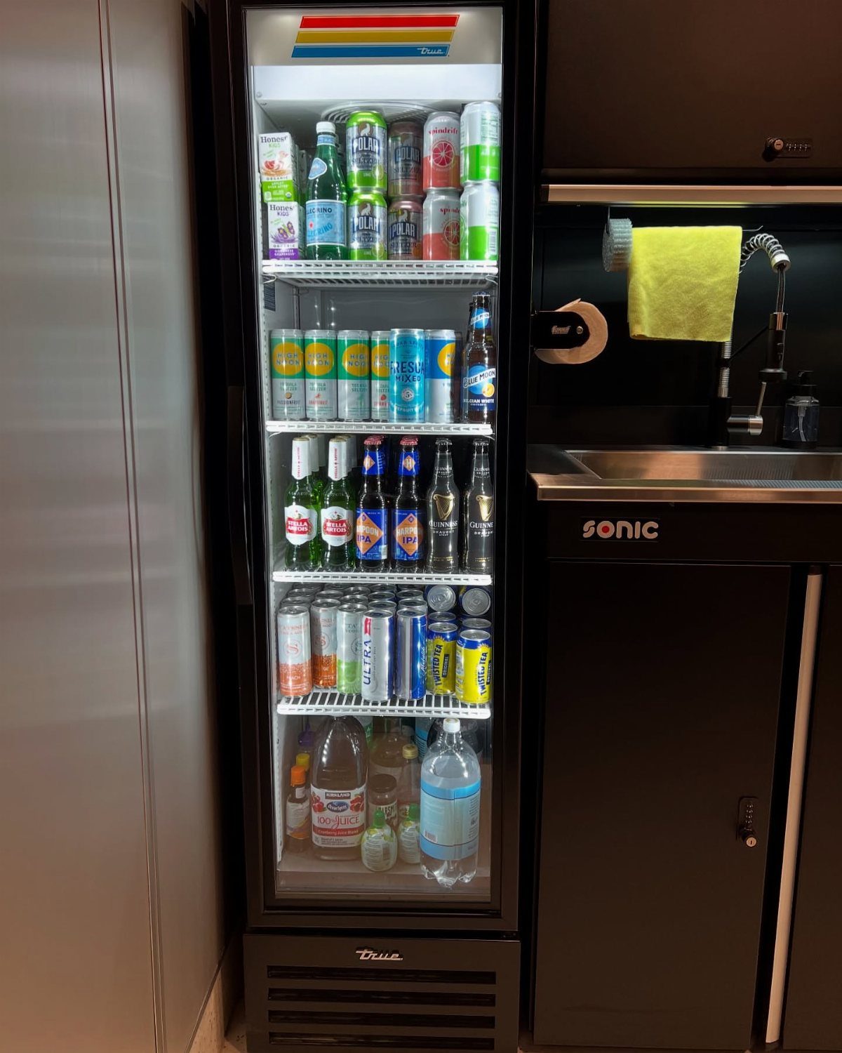 A tall black refrigerator stocked with various colorful canned and bottled beverages.