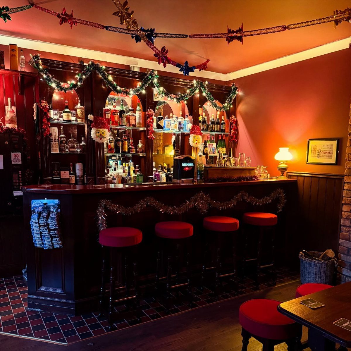 A dark wooden bar with red stools and festive holiday decorations and warm lighting.