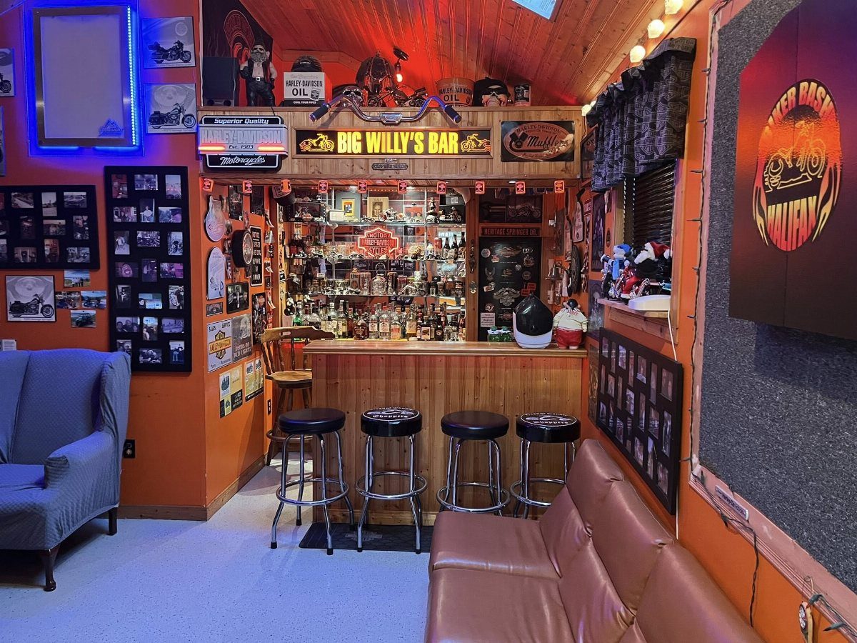 A motorcycle-themed home bar with wooden counters, black stools, and various biker memorabilia on orange walls.