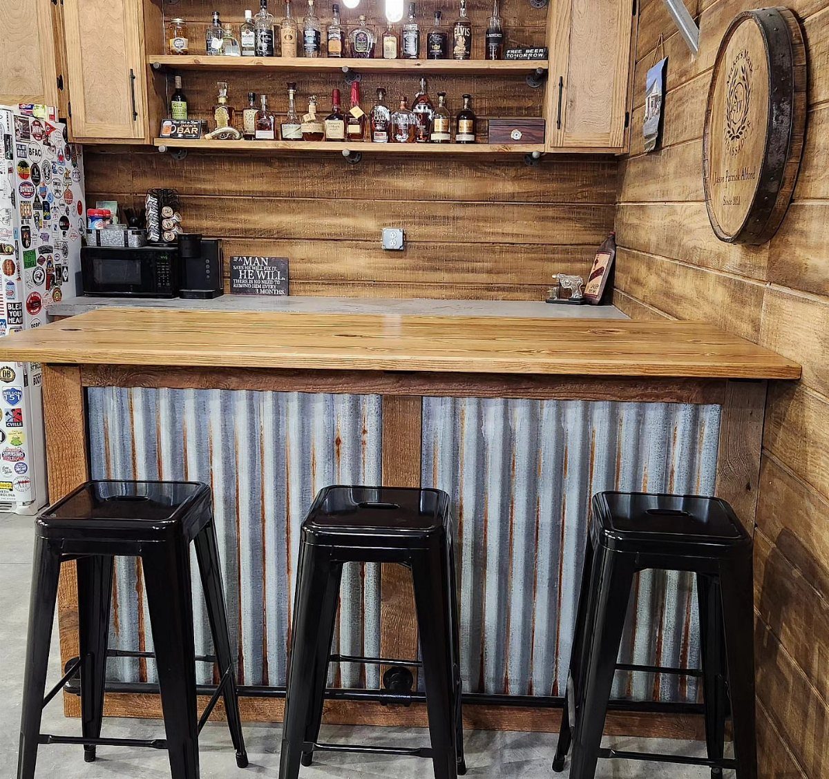 A rustic wooden bar with corrugated metal siding and three black metal stools.
