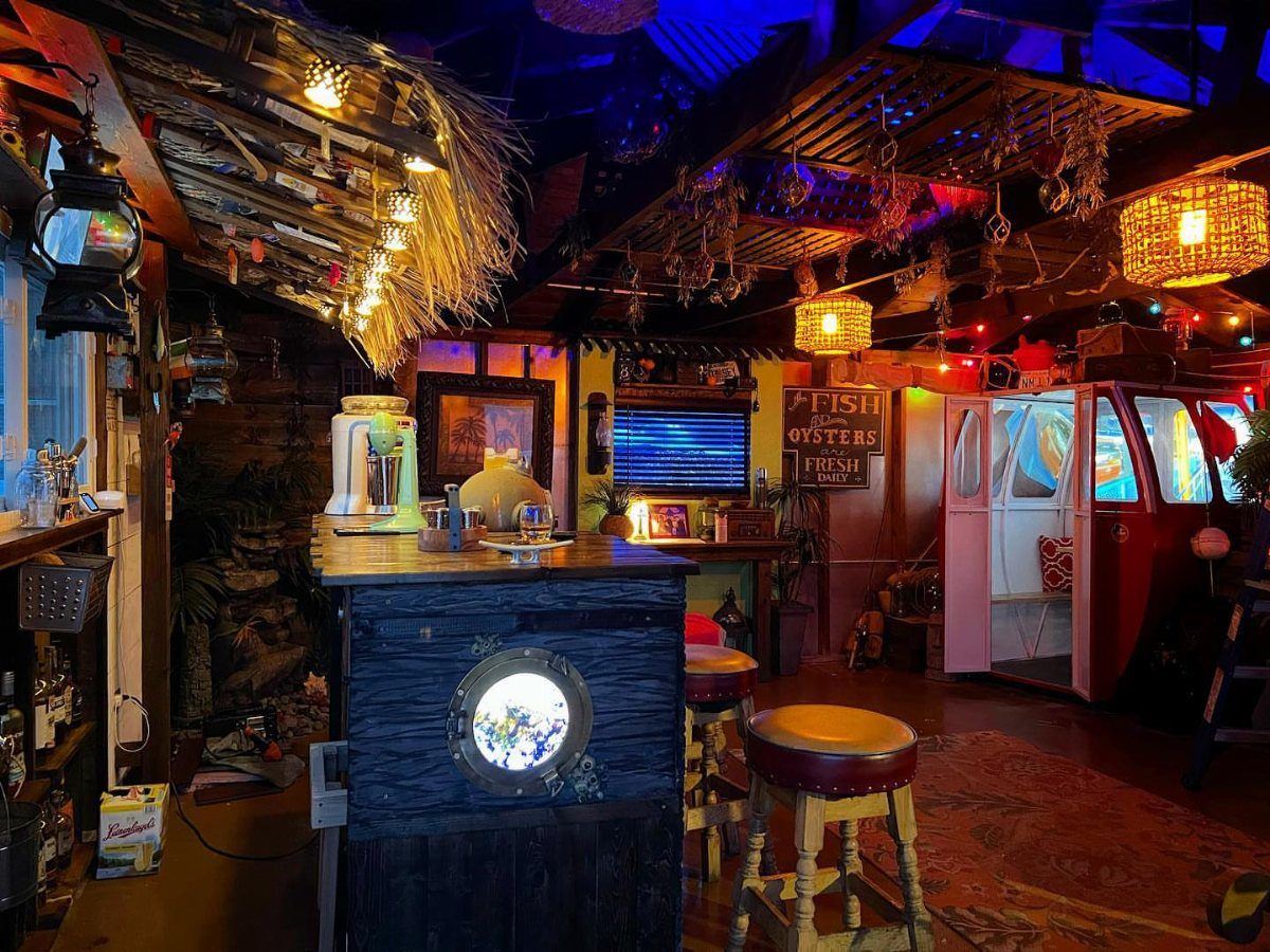 A tropical tiki bar with thatched roofing, colorful mood lighting, and wooden bar stools.