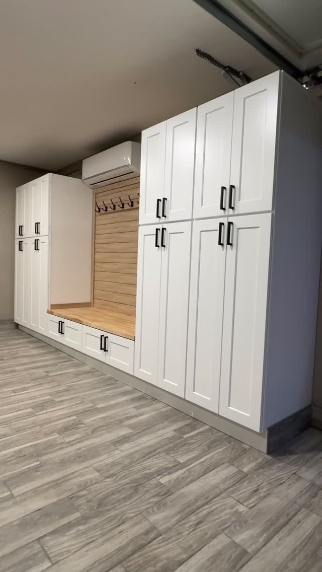 White built-in mudroom cabinetry with a wooden bench and coat hooks on a wood-paneled wall.
