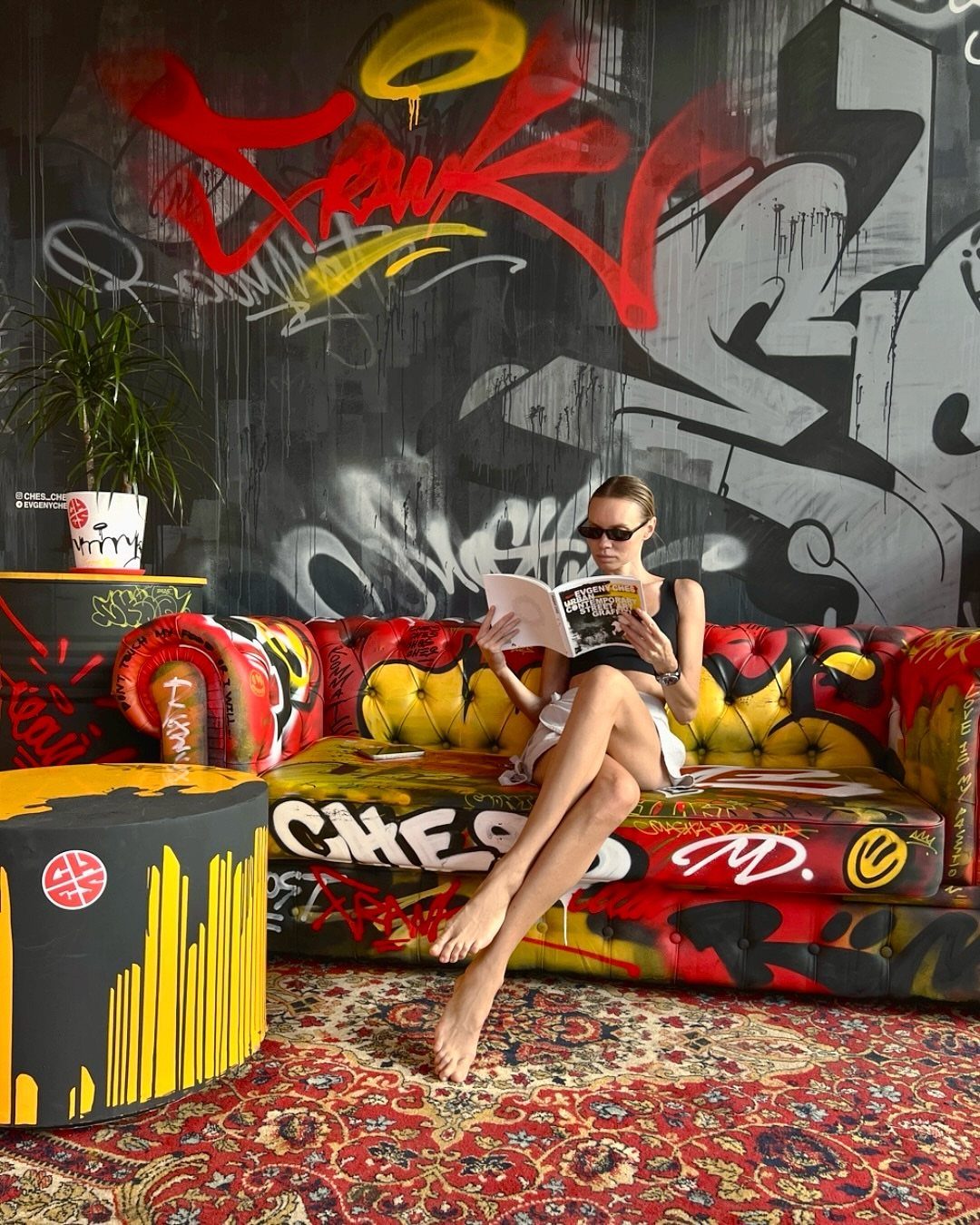 10 Garage Hangout Ideas for Comfortable Seating, Lighting, and More 10 Woman sitting on a graffiti-covered sofa in front of a large graffiti wall.