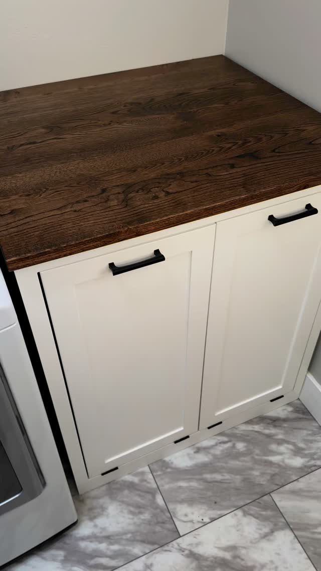 11 Garage Laundry Room Ideas for Storage, Style and Smart Layouts 6 White shaker-style cabinets with a dark wood countertop and black handles on marble tile.