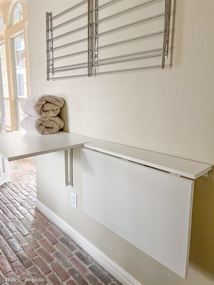 11 Garage Laundry Room Ideas for Storage, Style and Smart Layouts 2 A white fold-down wall-mounted workstation with folded towels and a metal drying rack above it.