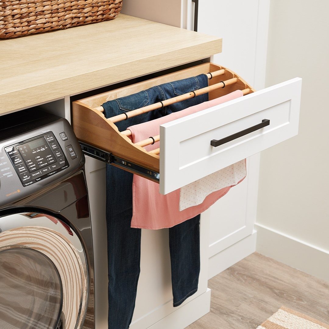 11 Garage Laundry Room Ideas for Storage, Style and Smart Layouts 1 A wooden pull-out drying rack extended from a white cabinet holding blue jeans and pink fabric.