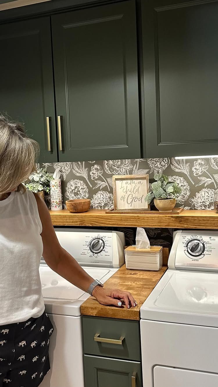 11 Garage Laundry Room Ideas for Storage, Style and Smart Layouts 3 Floral patterned wallpaper backsplash installed behind a wooden laundry room countertop and green cabinets.