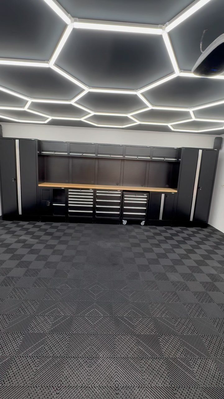 Black garage cabinets with a wooden workbench under glowing hexagonal ceiling lights.