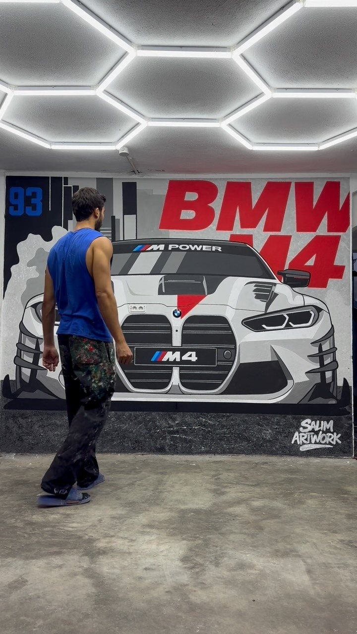 A man walking past a large BMW M4 car mural painted on a garage wall.