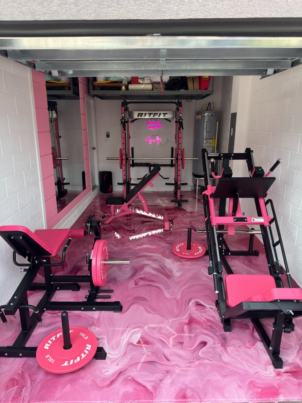 Pink and black weightlifting equipment arranged on a swirling pink epoxy floor inside a garage.