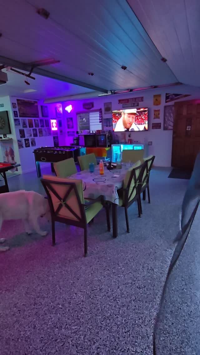 A converted garage game room with a dining table, pool table, and neon lighting.