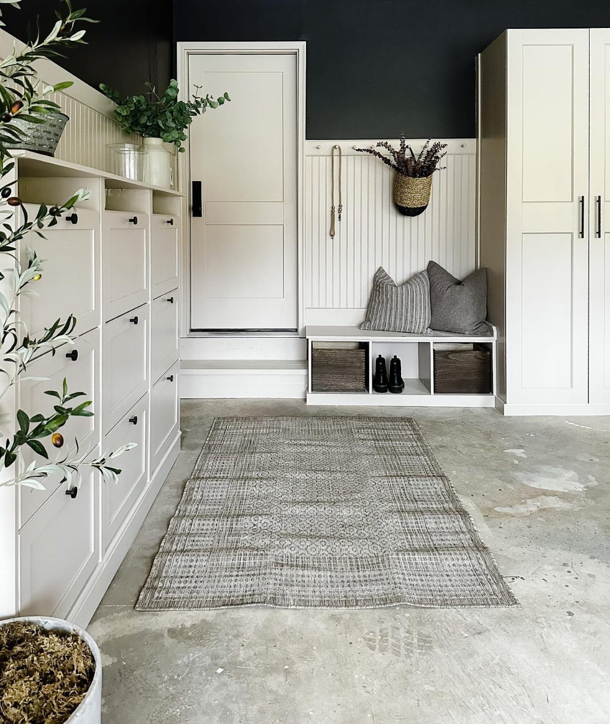 White built-in mudroom cabinetry and a storage bench with a grey rug on concrete.
