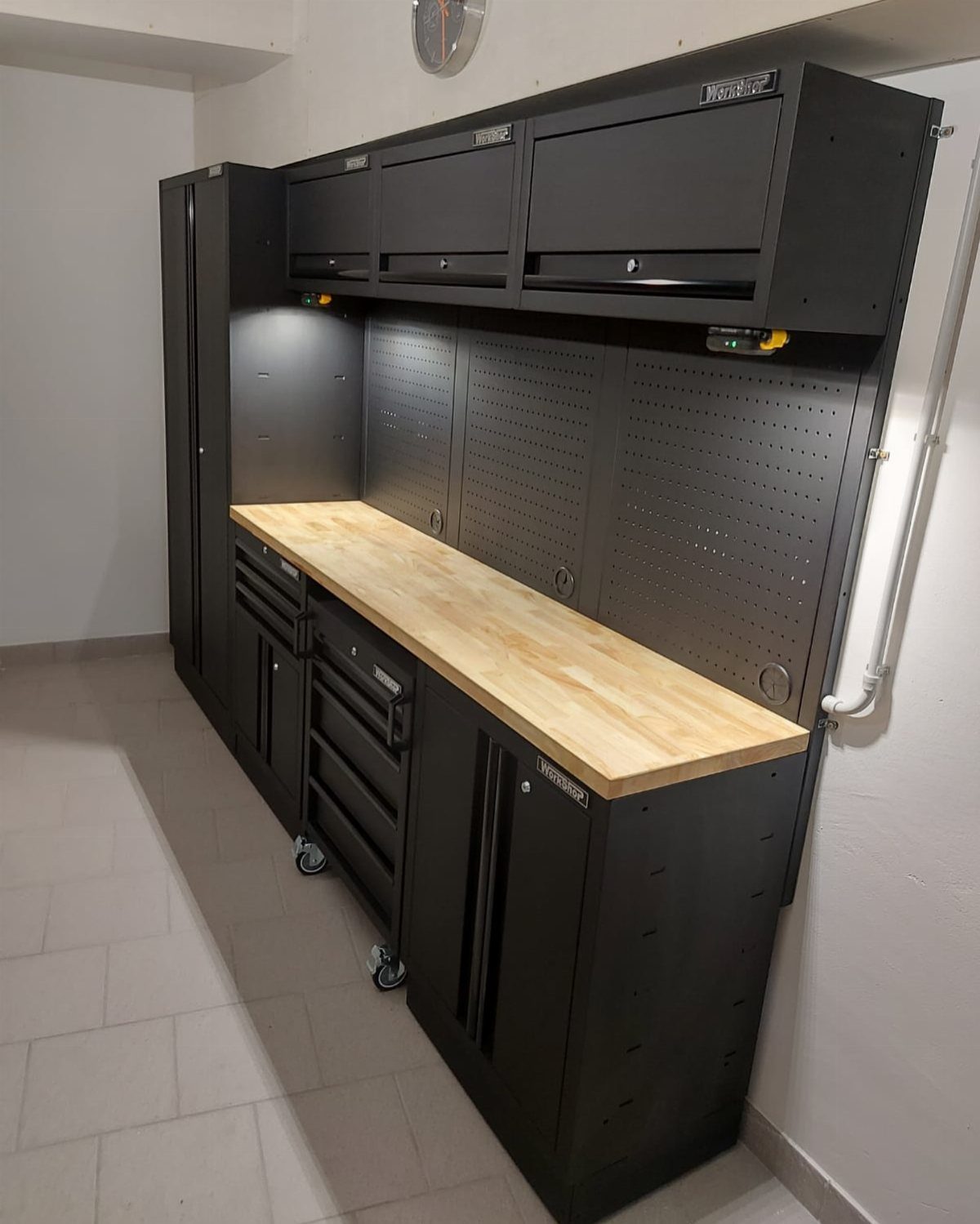 Black workshop storage unit with a wooden workbench and large pegboard backsplash against a white wall.