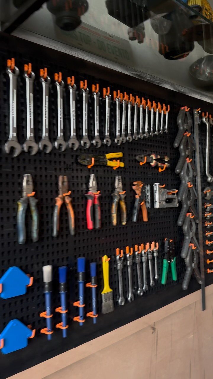 Various metal tools organized on a black pegboard with orange plastic holders.