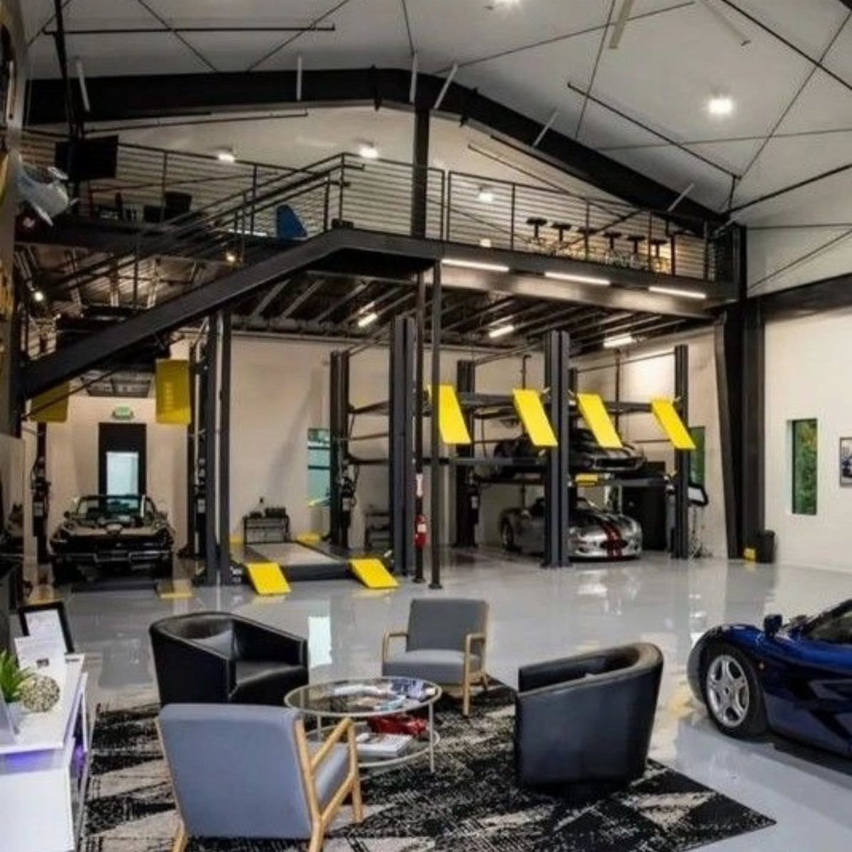 A luxury garage with a lounge area, sports cars, and a large black metal mezzanine loft.