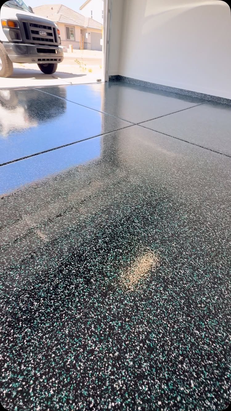 Shiny dark grey and teal epoxy flake garage flooring reflecting the sky and a vehicle.