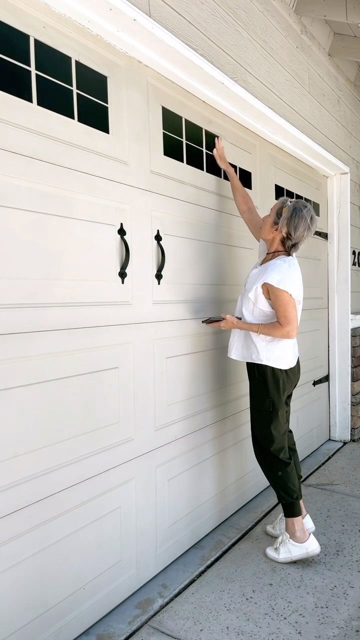 A woman standing beside a large white garage door with small windows and black handles.