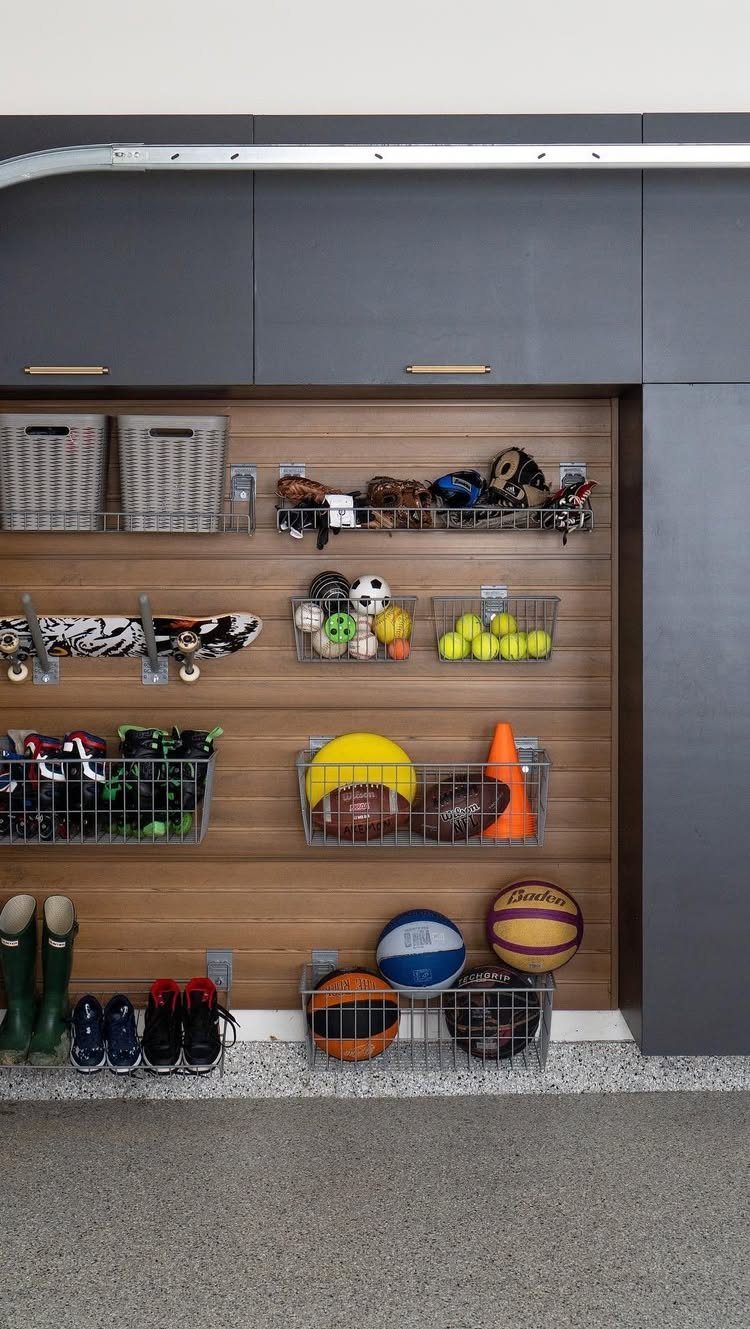 Wooden slatwall storage system holding various sports balls, equipment, and shoes in wire baskets.