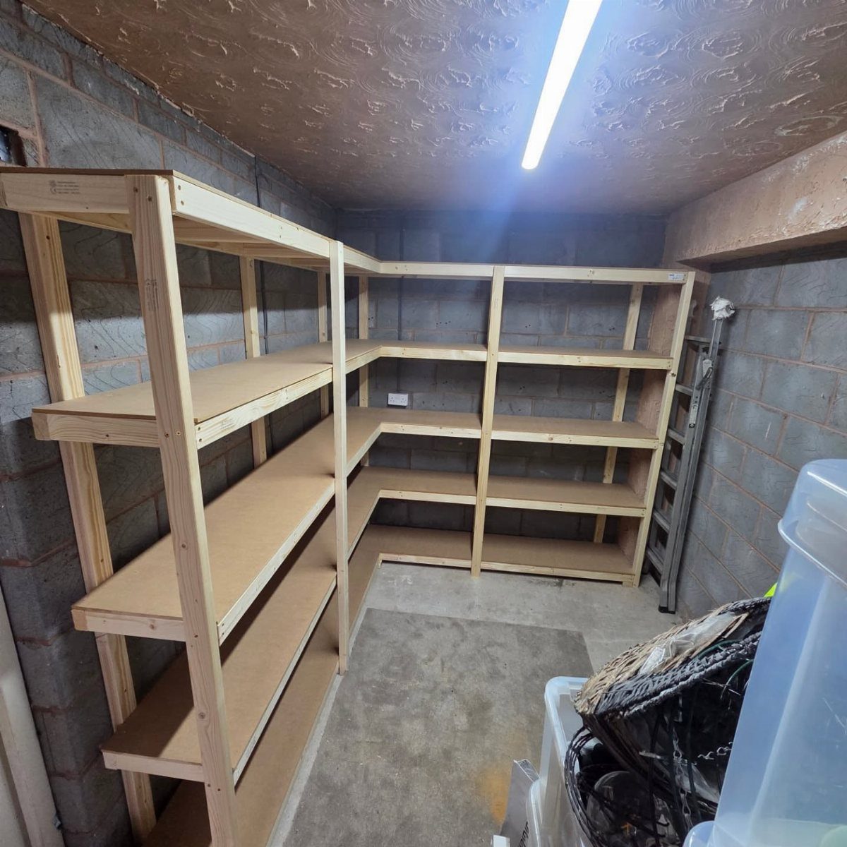 Newly built wooden L-shaped shelving units installed against cinder block walls in a garage.