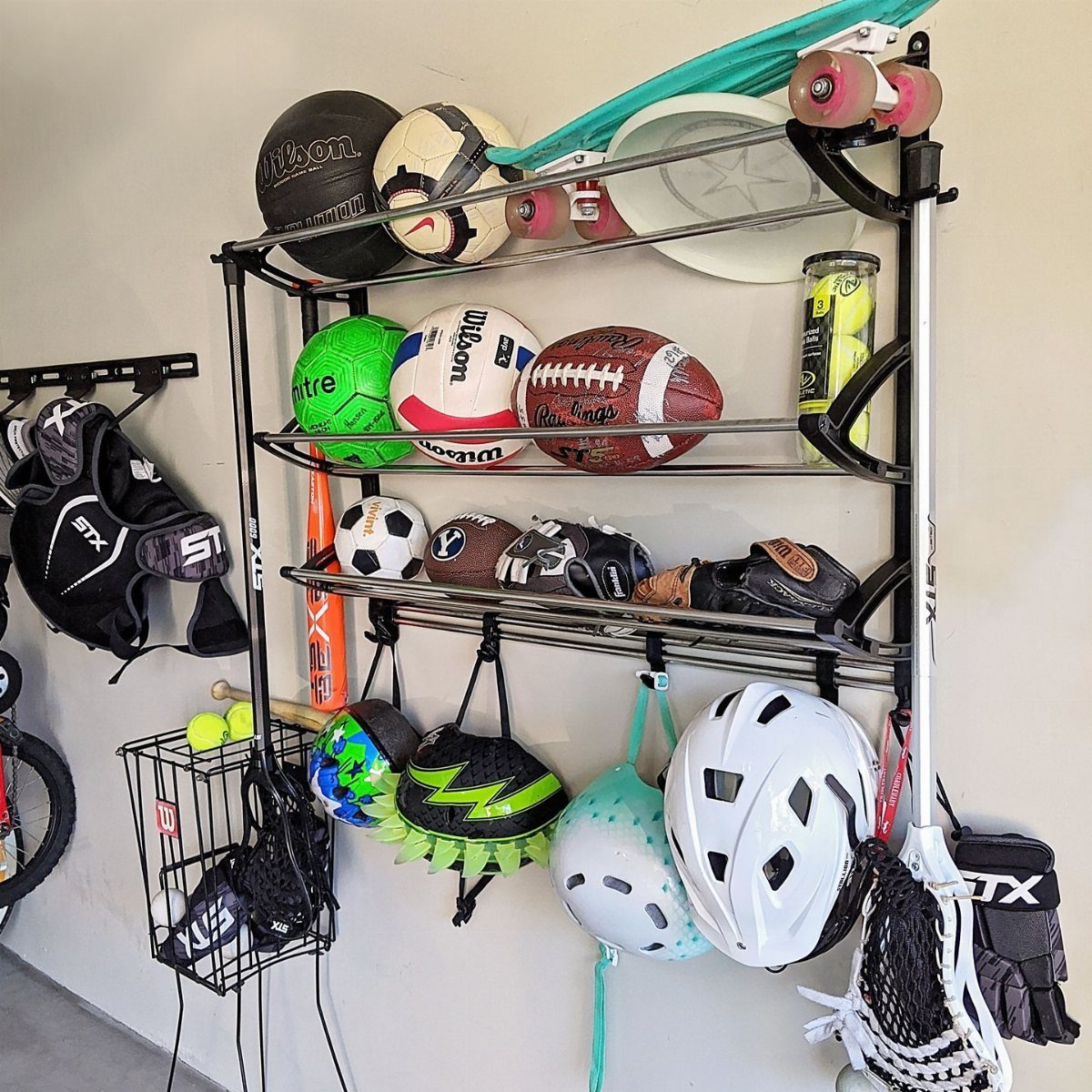 A black metal wall rack organizing various sports balls, helmets, and gloves in a garage.