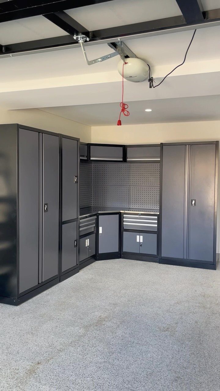 Dark gray metal garage storage cabinets and a workbench with a pegboard in a clean garage.