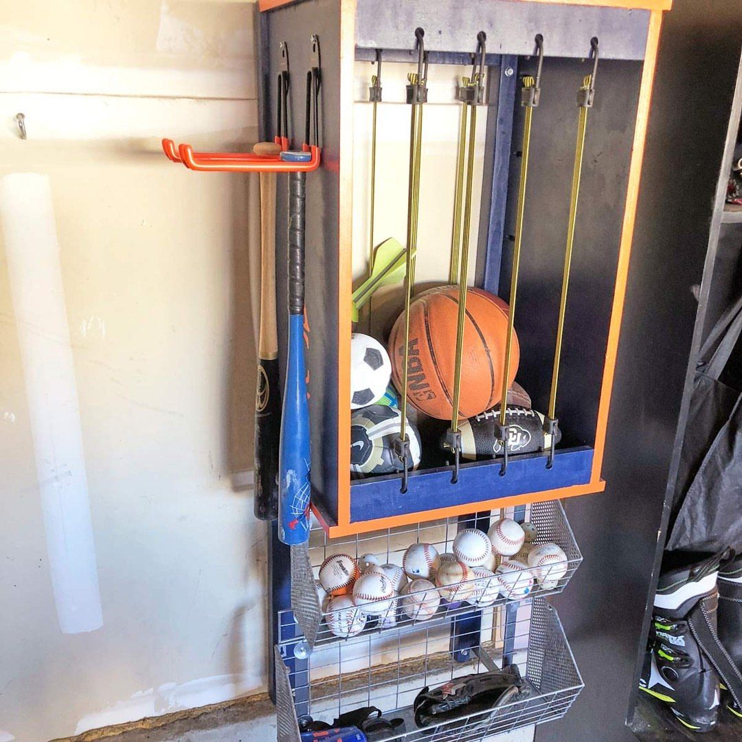 Sports balls secured by yellow bungee cords inside a blue and orange wooden storage unit.