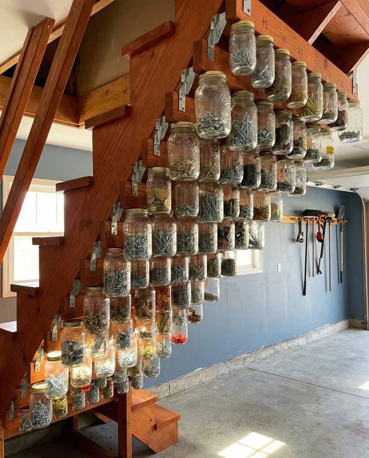 Mason jars filled with screws and nails mounted under wooden stairs in a garage.